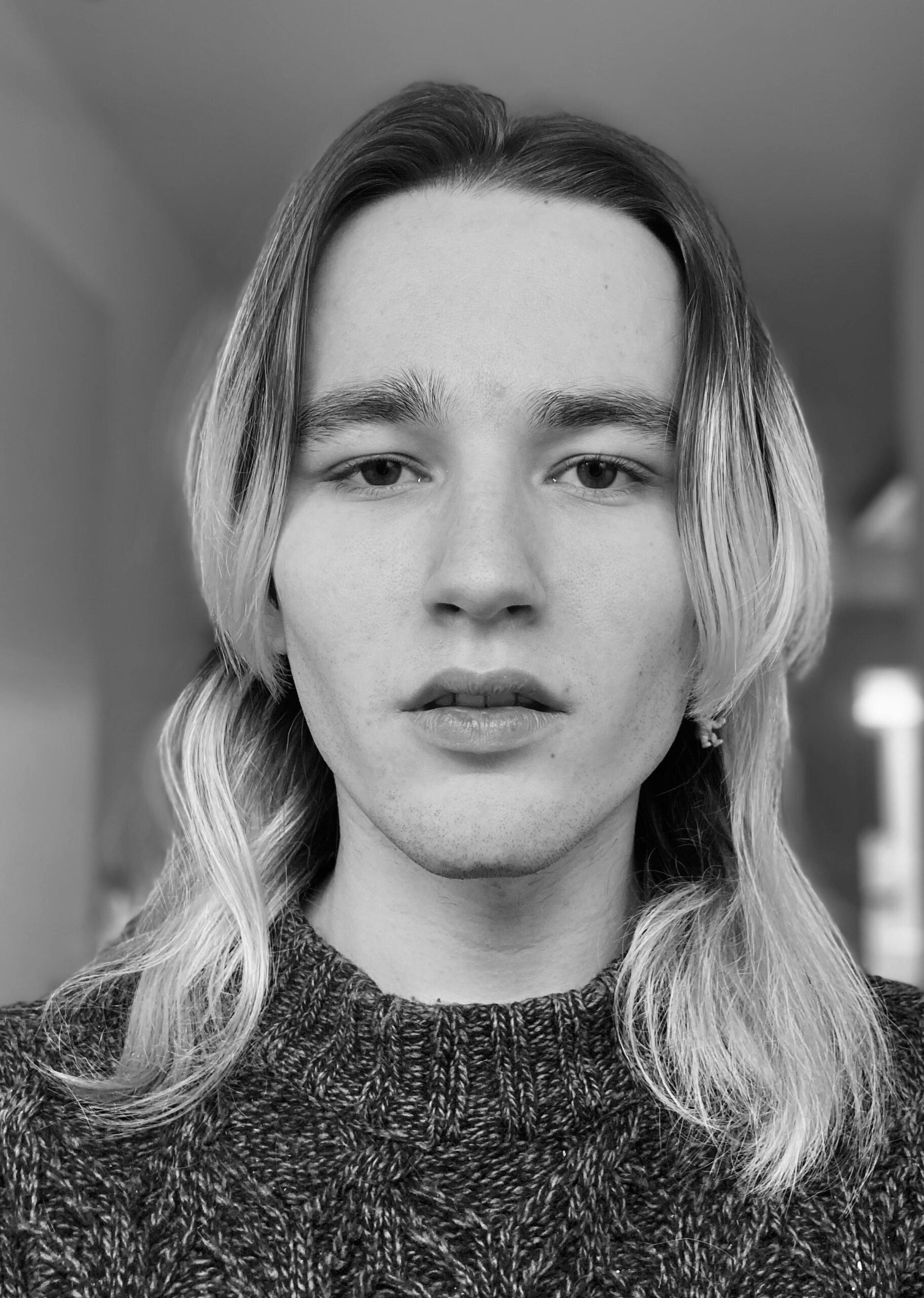 Schwarzweiß-Portrait, Louis Caspar Schmitt trägt lange blondierte Haare und einen Wollpullover und schaut direkt in die Kamera.