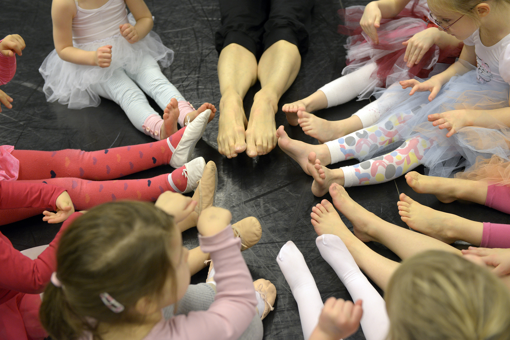 Von oben fotografiert Füße und Beine in Großaufnahme von Kindern und einer erwachsenen Person, die im Kreis sitzen.