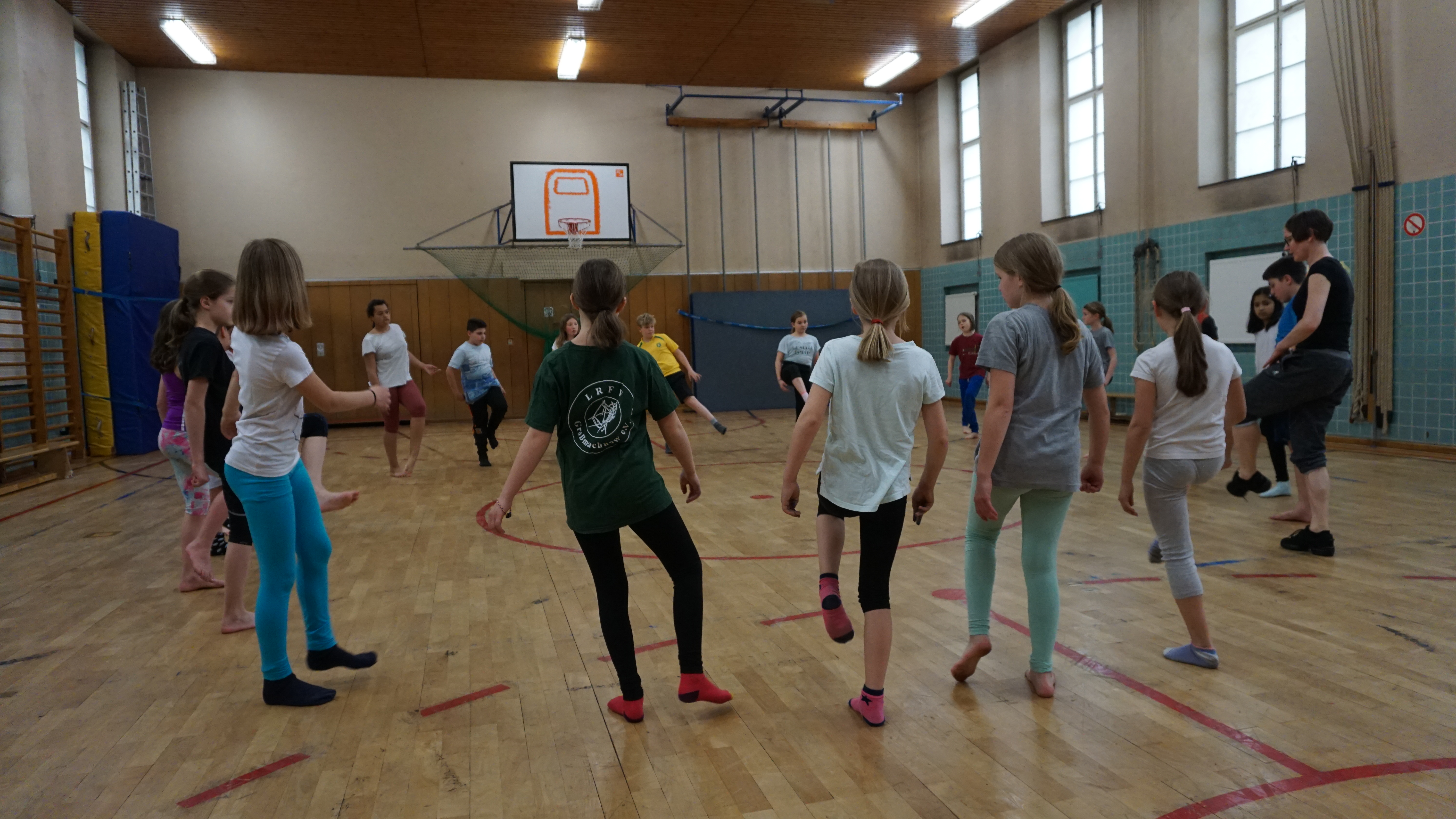 eine Kinderguppe in Sportkleidung steht im Kreis in einer Turnhalle