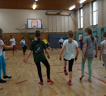 eine Kinderguppe in Sportkleidung steht im Kreis in einer Turnhalle