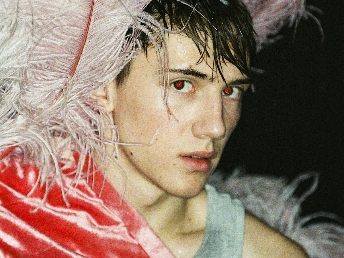 Tänzer Matthys de Beer trägt pinkfarbenen Federkopfschmuck und blickt verhalten in die Kamera.