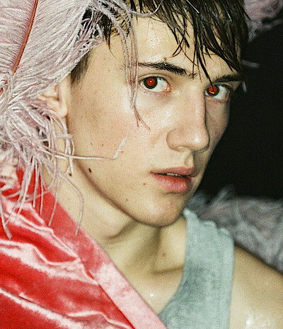 Tänzer Matthys de Beer trägt pinkfarbenen Federkopfschmuck und blickt verhalten in die Kamera.