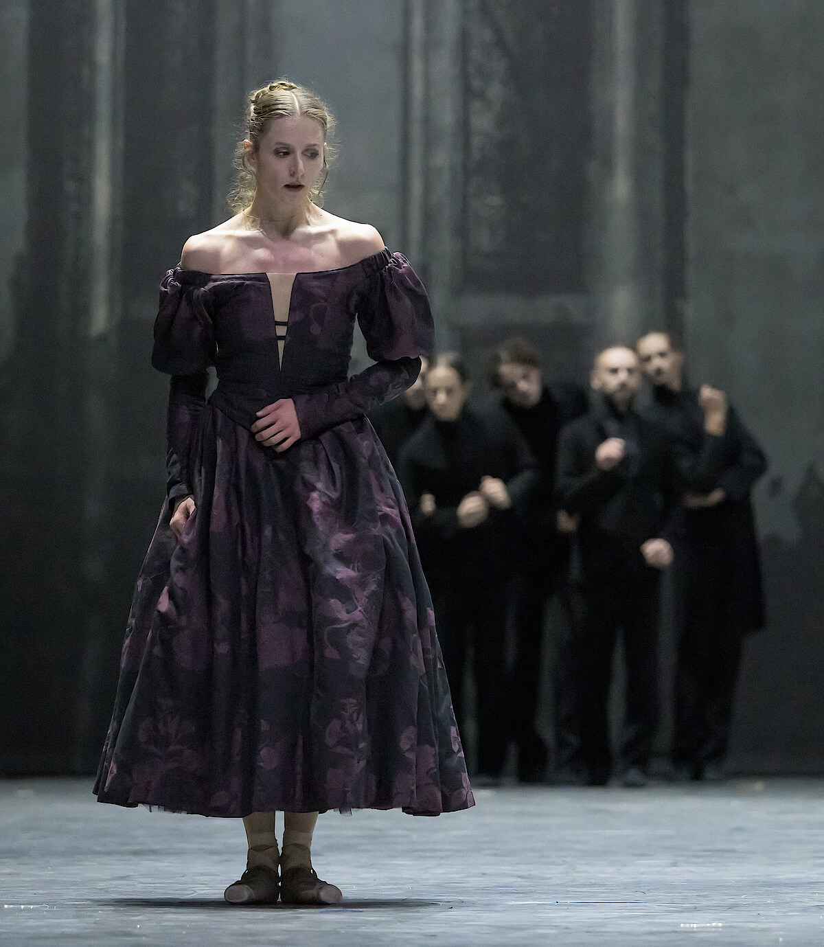 Weronika Frodyma als Emma Bovary steht angespannt am Bühnenrand und wird von Tänzern in schwarzen Anzügen beobachtet.