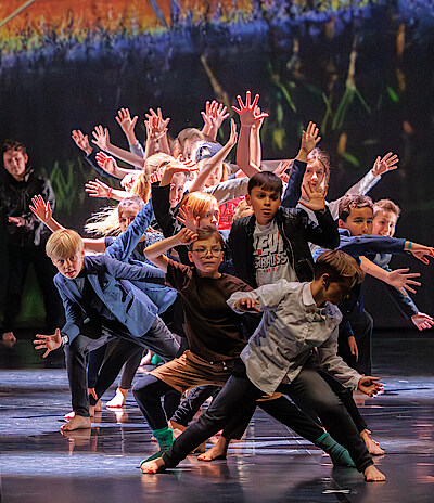 Kinder stehen auf der Bühne und strecken ihre Arme fächerförmig in die Luft