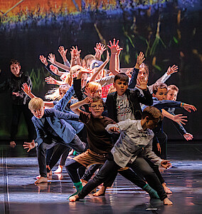 Kinder stehen auf der Bühne und strecken ihre Arme fächerförmig in die Luft