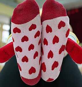 Zwei Füße in rot-rosa Socken mit Herzmotiv und zwei Babyfüße in roten Socken