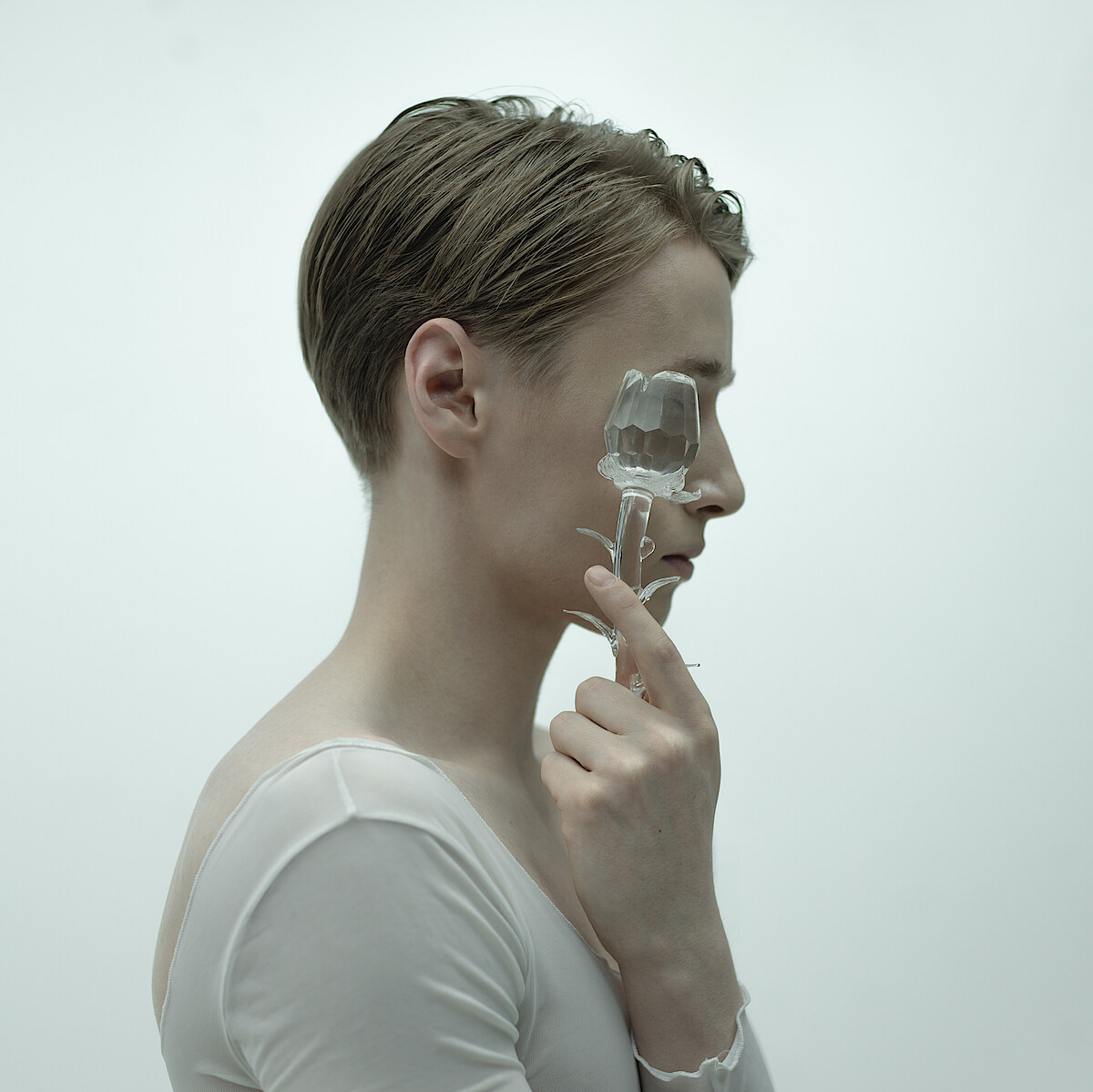 Kalle Wigle, im Profil vor neblig weißem Hintergrund, hält sich eine gläseren Rose vors Gesicht.