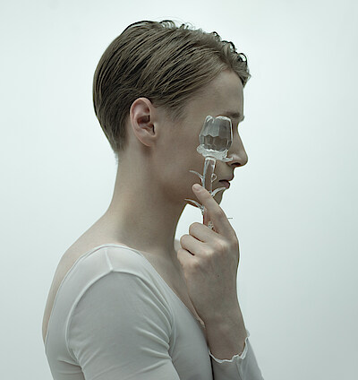 Saison 25/26 Kalle Wigle, im Profil vor neblig weißem Hintergrund, hält sich eine gläseren Rose vors Gesicht.