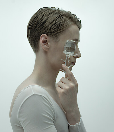 Kalle Wigle, im Profil vor neblig weißem Hintergrund, hält sich eine gläseren Rose vors Gesicht.