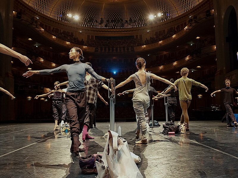 Tänzer*innen an der Stange auf der Bühne der Staatsoper Unter den Linden. Im Hintergrund das beleuchtete Auditorium.