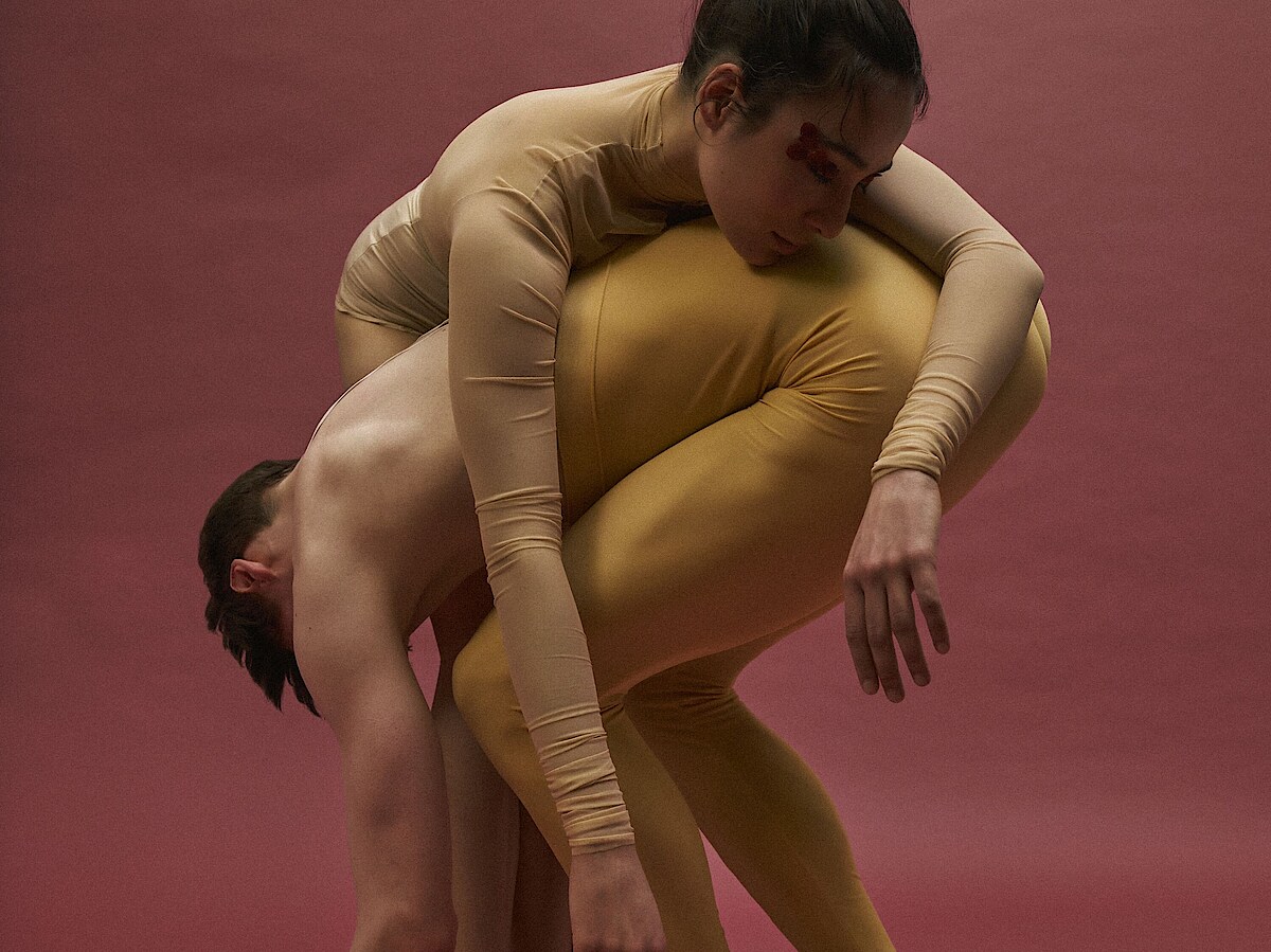 Spielzeit 24/25 Eine Tänzer in gelben Leggins lässt die Arme zu Boden hängen. Eine Tänzerin in weißen Leggins ist über seinen Rücken gebeugt.