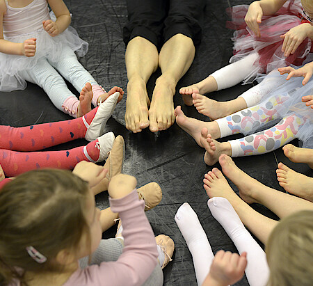 Von oben fotografiert Füße und Beine in Großaufnahme von Kindern und einer erwachsenen Person, die im Kreis sitzen.