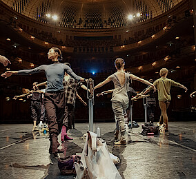 Tänzer*innen an der Stange auf der Bühne der Staatsoper Unter den Linden. Im Hintergrund das beleuchtete Auditorium.