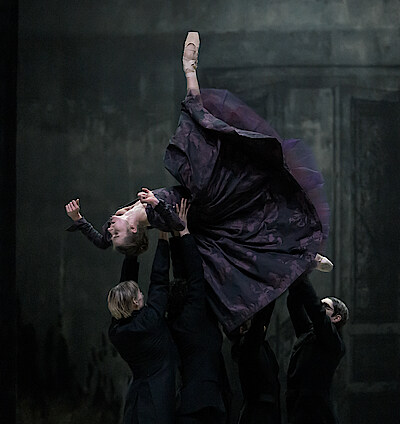 Tänzergruppe in schwarz trägt Solistin Weronika Frodyma als Emma Bovary, die ihren rechten Fuß in die Höhe streckt. 