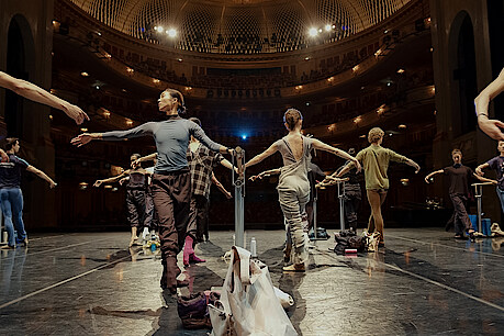 Tänzer*innen an der Stange auf der Bühne der Staatsoper Unter den Linden. Im Hintergrund das beleuchtete Auditorium.